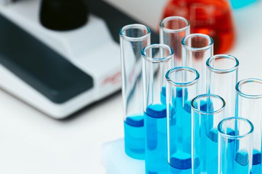 Scientific laboratory with microscope and colored test tubes with samples, close up photo
