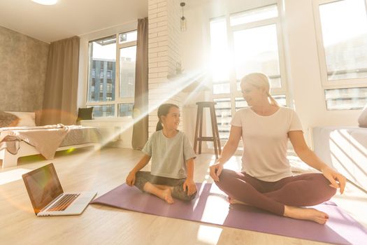 Mother and daughter practicing online yoga classes at home during the quarantine during the coronavirus pandemic. Family doing sports together online from home during isolation together at home