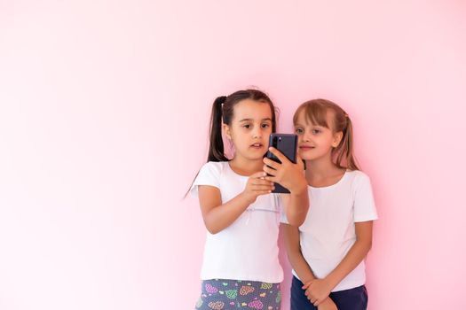 Two little girls playing with smartphones on a pink background