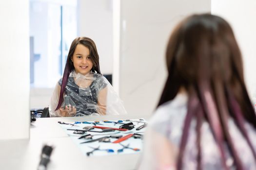 little girl dyes her hair purple in a hairdressing salon