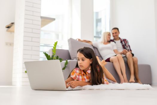 Beautiful cute charming little girl playing and surfing the internet on laptop smiling and lying down at home. Digital technology, internet usage and life style concept