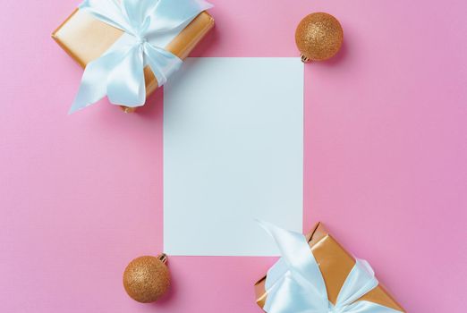 Christmas festive mock up with blank page, wrapped gifts and baubles on pink background