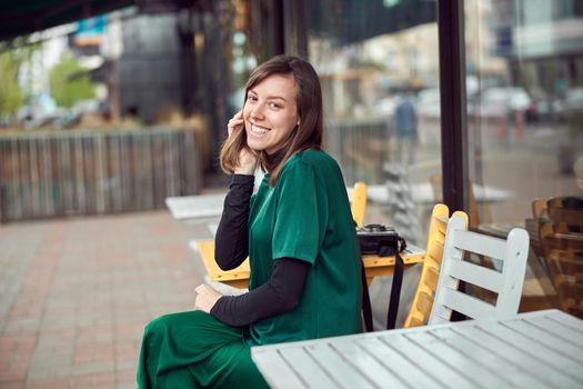 Portrait of cheerful young caucasian woman in green clothes that sitting outside cafe