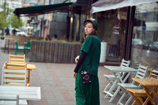 Happy young caucasian lady in green dress is walking near cozy cafe