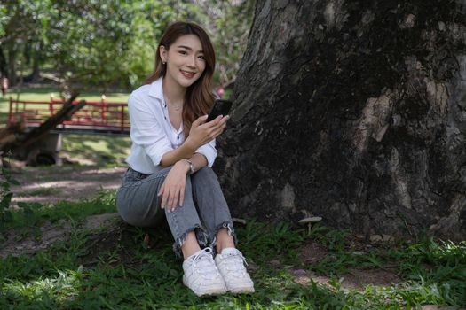 Image of pleased positive woman sitting outdoors in park and using cell phone.