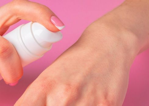 Female hand holding skincare product bottle on pink background