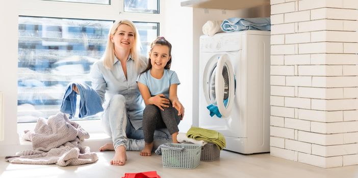 family mother and child girl little helper in laundry room near washing machine and dirty clothes