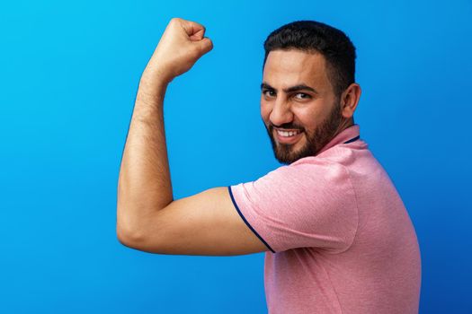 Hispanic man with beard wearing casual t-shirt showing arms muscles against blue background, close up