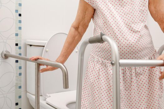 Elderly woman holding on handrail in toilet.