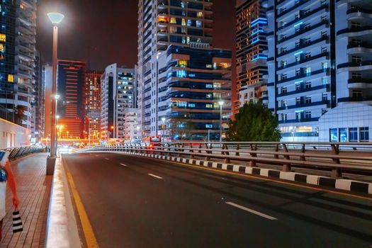Empty asphalt road with modern buildings at night in Dubai, UAE