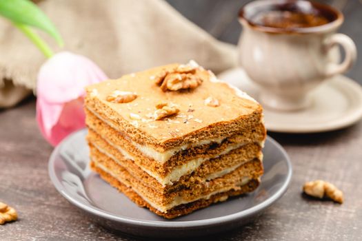 Slice of layered honey cake on a plate with cup of coffee and tulip flower, selective focus