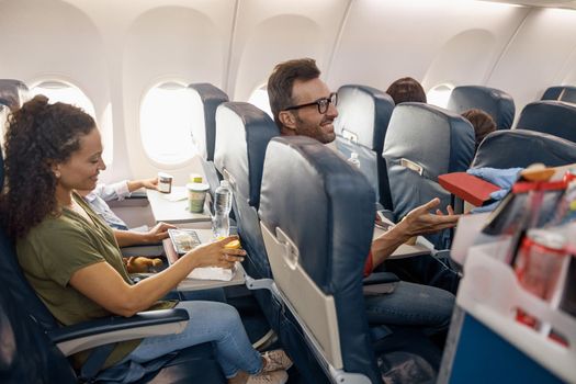 Cheerful passengers smiling, waiting for female flight attendant serving lunch on board. Travel, service, transportation, airplane concept