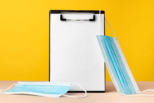Clipboard with copy space and medical face mask against yellow background