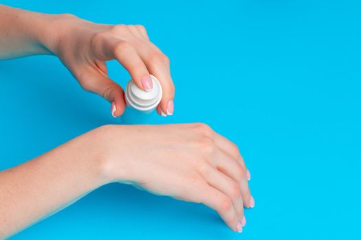 Female hand holding skincare product bottle on blue background