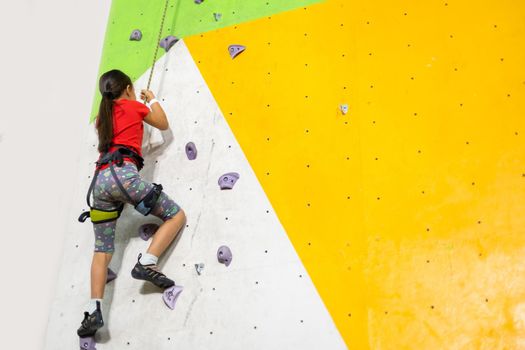 Sporty little girl climbing artificial boulder on practical wall in gym