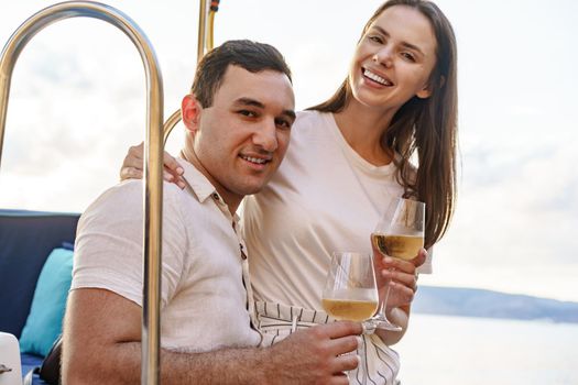 Young loving couple sitting on the yacht deck and drinking wine together