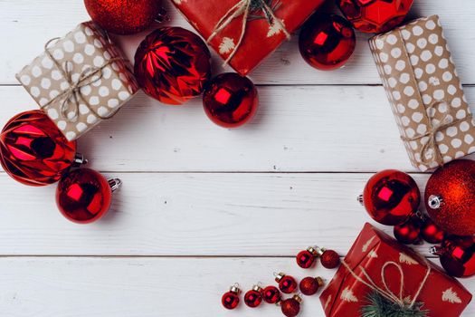 Packed small Christmas gifts and red baubles on white wooden board top view