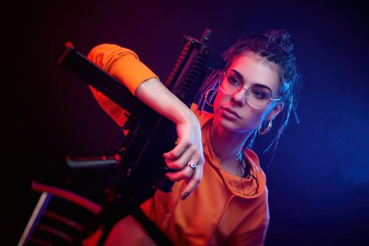 beautiful face brunette in a red jumpsuit with a short barrelled machine gun on a dark background in neon light