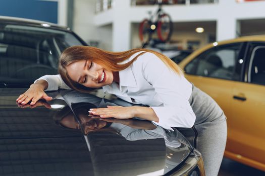 Beautiful young woman touching her new car with pleasure and joy