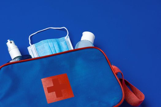 First aid kit with mask and sanitizer on blue background close up
