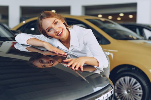 Beautiful young woman touching her new car with pleasure and joy