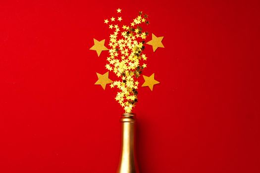 Champagne bottle with sparkling confetti on red background flat lay top view