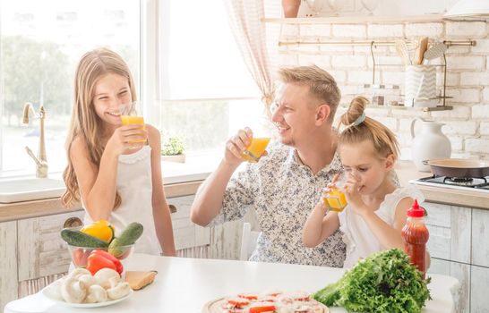 Dad with two daughters drinks orange juice in the kitchen