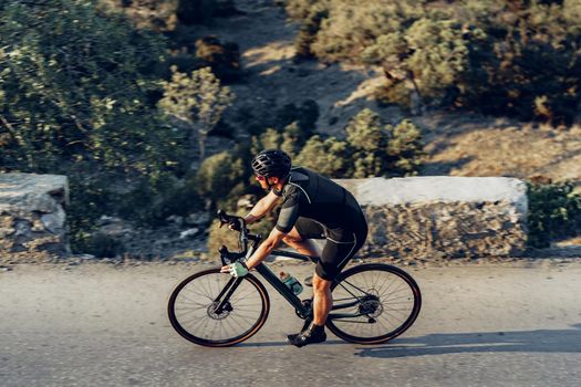 Man cyclist pedaling on a road bike outdoors in sun set at coastal road