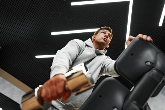 Determined handsome young male working out in gym with dumbbells, close up