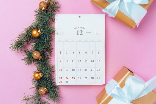 Calendar page of december with festive decorations on pink background, top view