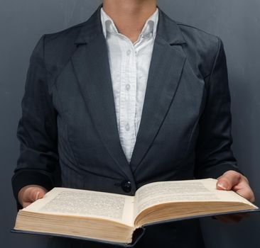 Unrecognizable teacher reading a book near the blackboard, front view
