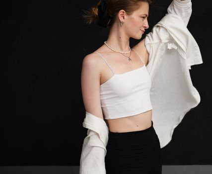 Caucasian girl in white blouse posing in studio on black background
