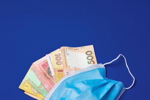 Medical face mask and Ukrainian hryvnia banknotes on blue background, close up