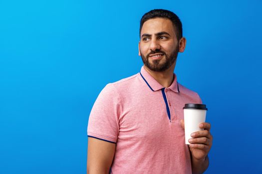 Young handsome man holding coffee to take away against blue background, close up