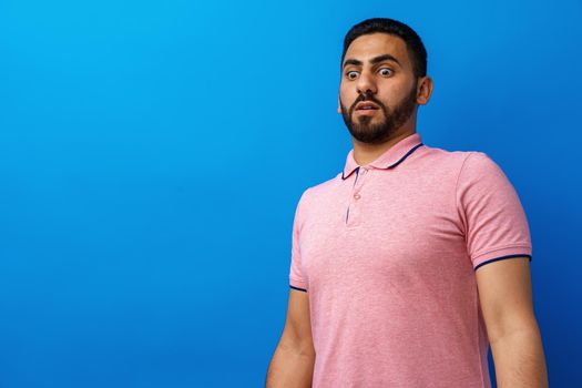 Young man nervous and scared looking at something against blue background, close up