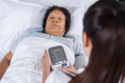female nurse checking blood pressure of a senior woman on bed