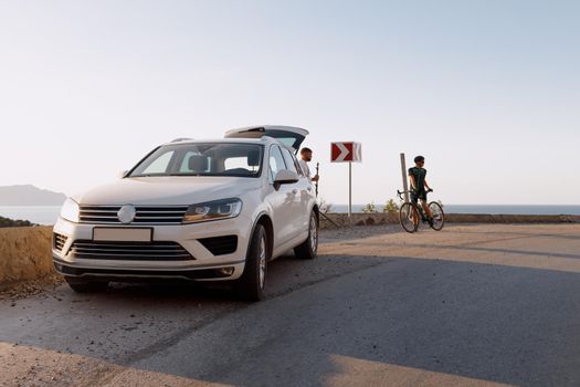 White crossover car on the coastal road and man with bicycle starting his ride
