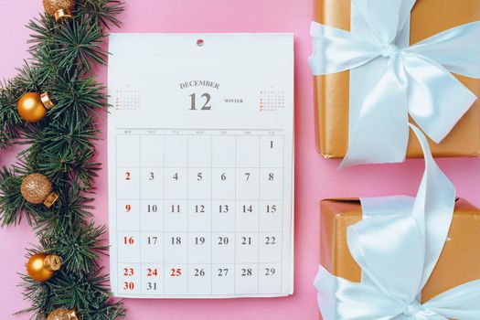 Calendar page of december with festive decorations on pink background, top view