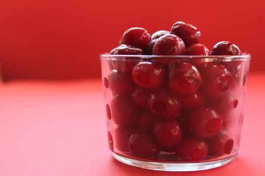 cherry in a glass on a pink red background with a place to text the view from the side close-up of the copyspace.