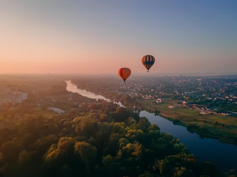 Two colorful air balloons flying over green park and river in small european city at summer sunrise, Kiev region, Ukraine