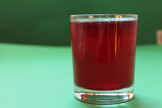Red drink juice or compote in a glass on a green background with a place for text and copyspace.
