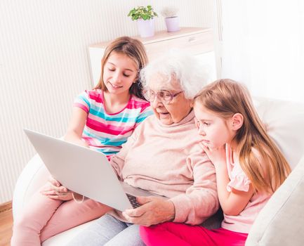 Great-grandmother with granddaughters watching laptop together