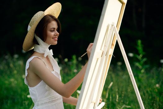 Woman in white dress paints a picture on nature easel. High quality photo