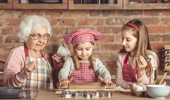 Grandma and granddaughters are spreading dough using a rolling pin