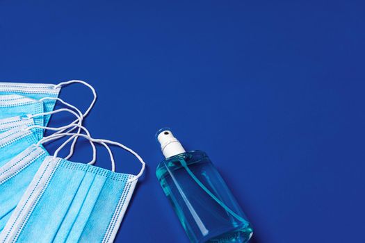 Pile of medical face masks with hand sanitizer on blue background close up