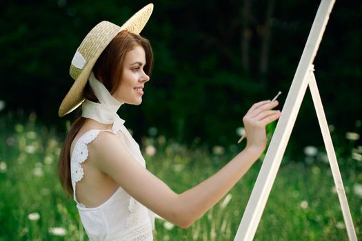 Woman in white dress paints a picture on nature easel. High quality photo