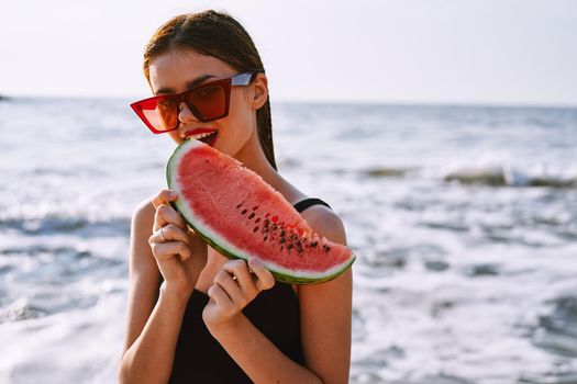 cheerful woman in sunglasses eating watermelon by the ocean. High quality photo