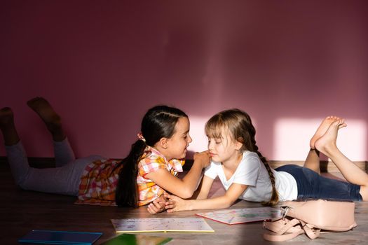 Little girls reading a book in living room. Smart schoolgirls doing their homework after school. Education and distance learning for kids. Homeschooling during quarantine. Stay at home entertainment.