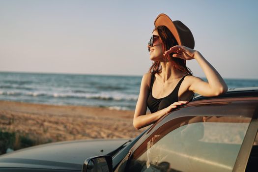cheerful woman in sunglasses and a hat on the ocean near the car. High quality photo