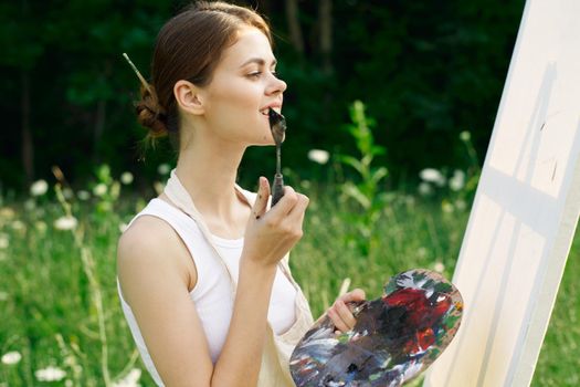 woman artist outdoors with palette of paints paints a picture. High quality photo